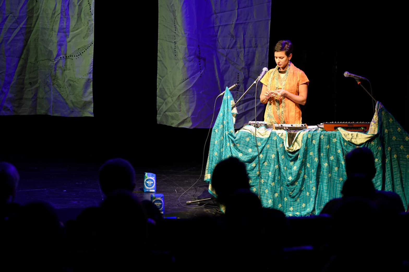 woman on stage behind a table covered in a green and gold saree